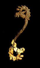 
La tombe d'un prince scythe (Kazakhstan), les objets d'art scythe. Barrette de mors à protomés d'élan, l'élan est coiffé de grands bois en palette festonnés à l'arrière et lobés à l'avant ; son museau aux grosses lèvres pend de manière caractéristique et on a gardé le détail de l'appendice charnu qui pend sous la mandibule. L'oreille, allongée vers l'arrière, trace un pont entre la tête et les bois, permettant au sculpteur de donner plus de solidité à son œuvre. Ces protomés d'élans sont obtenus par des procédés de stylisation savants qui dégagent l'essentiel du thème sélectionné. Le contraste entre la tête encore revêtue d'or et celle qui a perdu son enrobage d'étain est grand : la qualité de l'ouvrage n'est perceptible que sur la seconde
